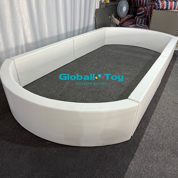 Side view of a soft play oval ball pit with white padding.