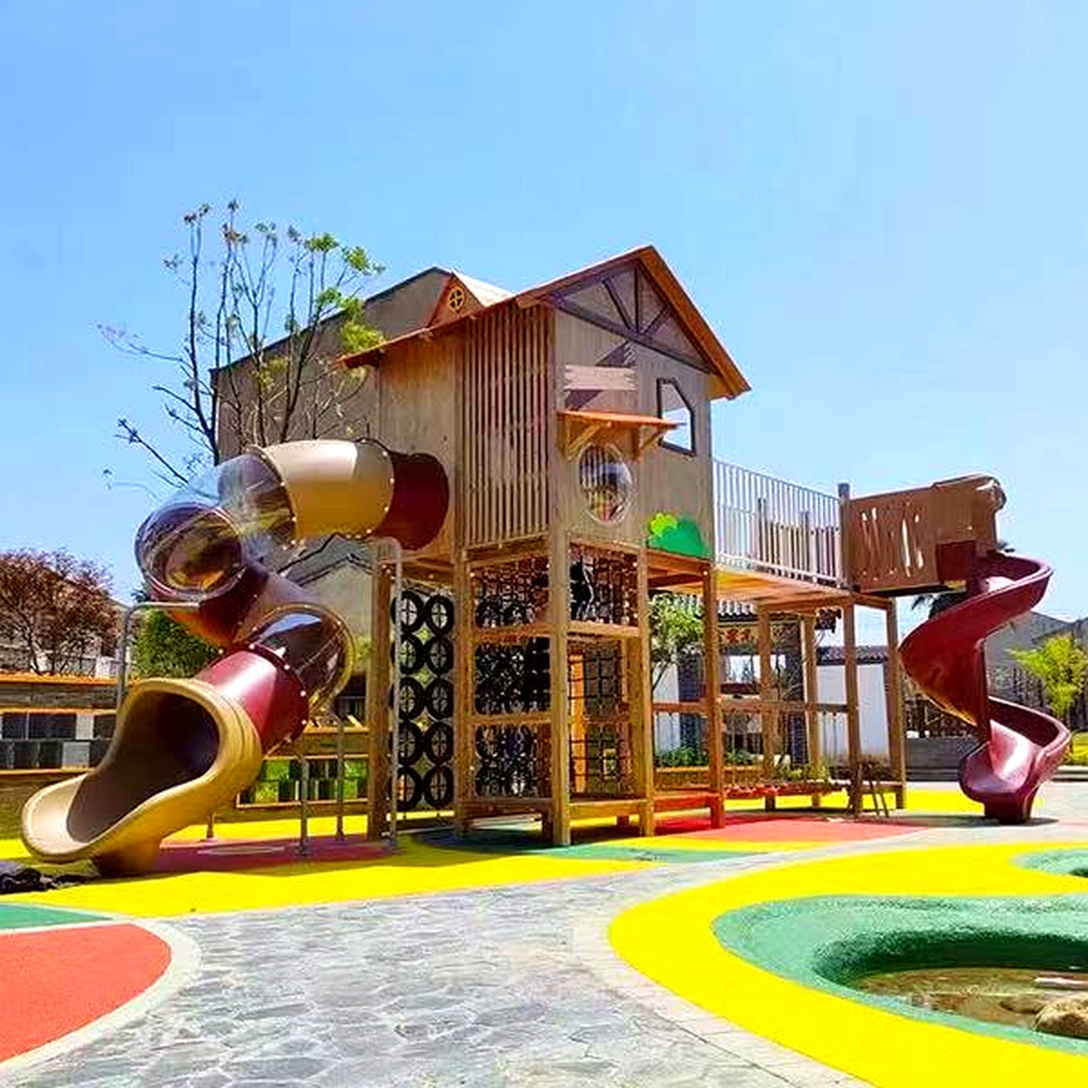 Maison de terrain de jeu en bois avec toboggan en spirale de tube transparent et filets d'escalade sur un sol en caoutchouc coloré, un équipement de parc extérieur